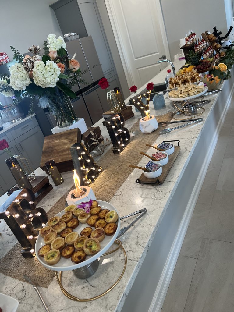 Elegant baby shower buffet setup with pastel desserts, floral arrangements, & champagne flutes by Creative Catering Naples.