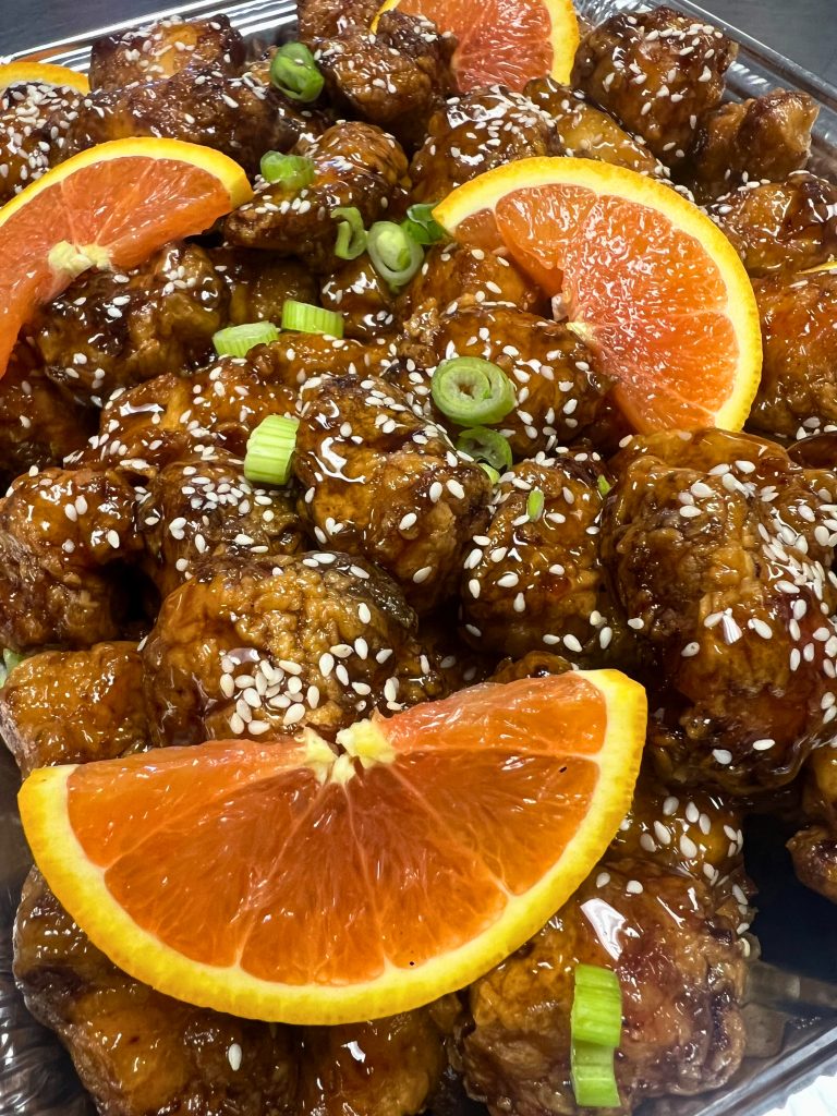 Catered orange chicken dish by Creative Catering Naples, featuring crispy chicken in citrus glaze with fresh garnish.