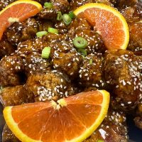 Catered orange chicken dish by Creative Catering Naples, featuring crispy chicken in citrus glaze with fresh garnish.