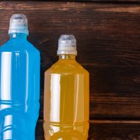 Two bottles of orange and blue on a dark wooden background, restoring water and salt balance after sports training, close up.