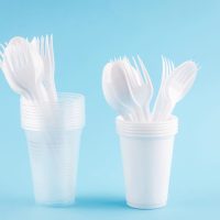 White Disposable cups, plates, forks, knives on light green blue background close-up - Environmental problem concept, copy space